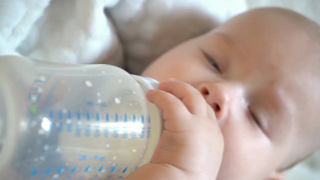 Cute baby boy holding  to the bottle and drink from it milk, 4K