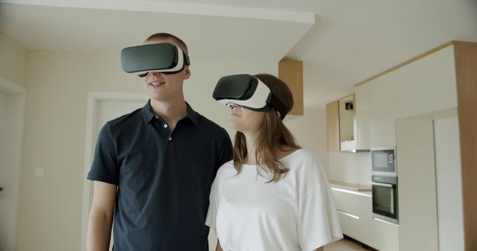 Young couple wearing VR headsets in new apartment. Young man and woman viewing new apartment and wearing virtual reality headsets.