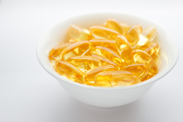 Dietary supplementation. Capsules of fish oil in the white bowl, light background