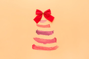 Beautiful Christmas tree made of lipstick strokes and bow on color background