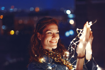Young redhead woman holding fairy lights outdoors