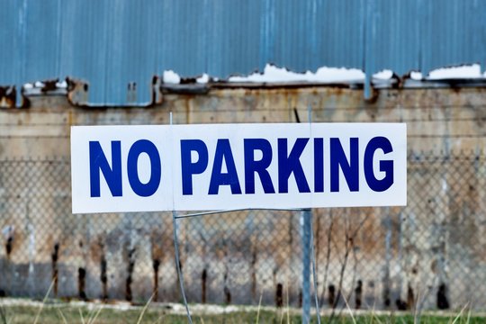 No Parking sign painted in blue letters with derelict building in the background.