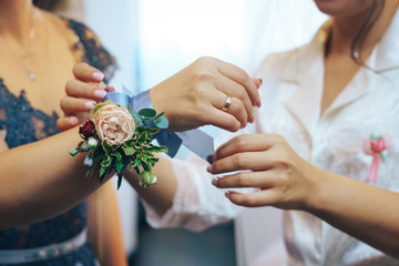 Bride places a flower corsage on the hand of her made of honour