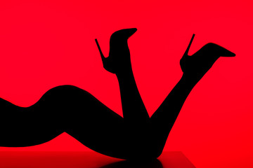 black silhouette of sensual woman in heels posing on table isolated on red