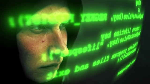 Close-up of male hacker working on a computer for cyber attack while green binary hacking code characters running in front of him in a dark office room. Motion graffic. 4K (UHD)