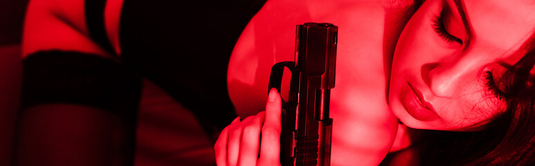 panoramic shot of beautiful seductive criminal woman in bodysuit holding gun on red