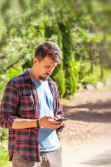 Young handsome Caucasian man writes on the phone, chatting, sending messages. Man in the park waiting for a date