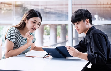 Two young teenagers talking about project, doing work together,at meeting room,blurry light around.