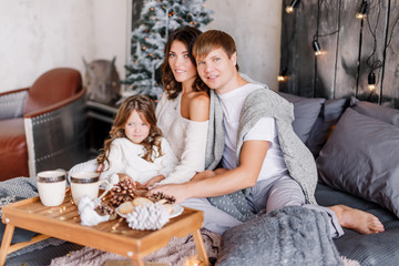 Obraz na płótnie Canvas Happy loving family mother, father and child on Christmas sit on the bed with a drink. New year 2020. Parents play with their daughter.