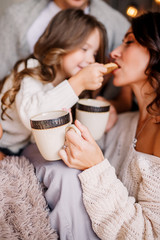 Happy family mother, father and child on Christmas sit on the bed with a drink. Little girl feeds mom is cookies. Mother is sitting on the floor. New year 2020.