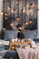 Cozy room with table, a cup on the bed, marshmallow and cookies, cozy knitted blanket. New Year 2020, flat lay. Christmas composition with a mug, tray, a deer and a Christmas tree.
