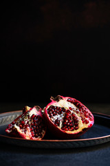 Sliced juicy pomegranate fruit on a vintage metal plate. Front view, black background, copy space