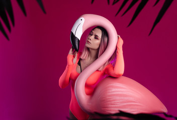 a girl in a bright bodysuit poses with a large Flamingo figurine