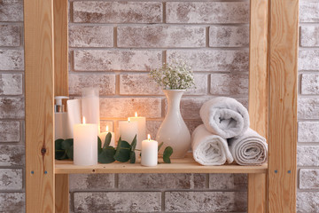 Glowing candles with cosmetics and towels on shelf