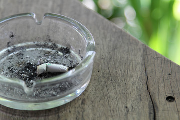 Cigarette butt with ash in glass ashtray on wooden table.