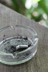 Cigarette butt with ash in glass ashtray on wooden table.