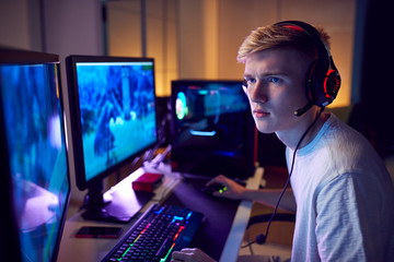 Fototapeta na wymiar Teenage Boy Wearing Headset Gaming At Home Using Dual Computer Screens