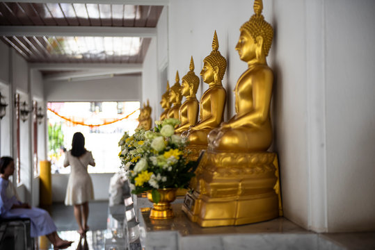 Peaceful gold sitting Buddha images placed rounded a terrace of Wat Pathum Wanaram, Bangkok, Thailand. Buddha statue posing “The attitude of subduing Mara”. People come and meditate in front.