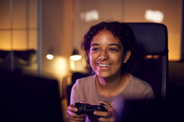 Teenage Girl With Game Pad Sitting In Chair and Gaming At Home  © Monkey Business