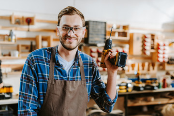 happy carpenter in goggles and apron holding hammer drill