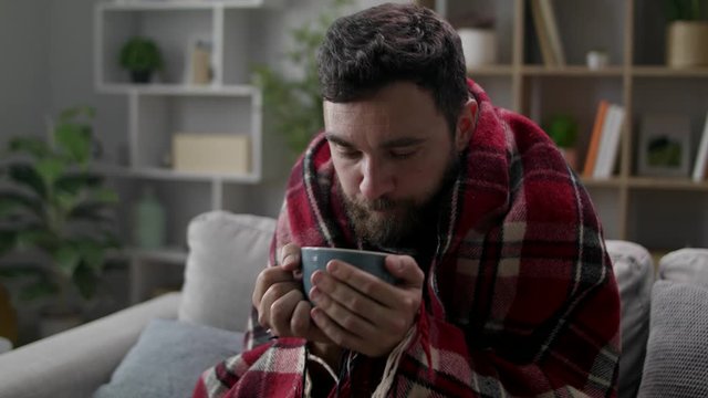 Cold man drinks tea on the sofa in the living room