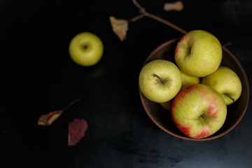 Yellow fresh apples in a bowl standing on black table background. Top view, copy space
