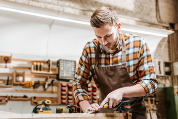 bearded carpenter holding chisel while carving wood in workshop