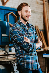 Obraz premium cheerful carpenter standing with crossed arms in workshop