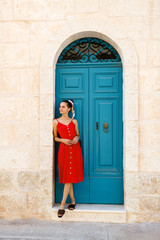 Fototapeta na wymiar Happy young brunette woman in a red dress outdoors on a background of blue doors. Old city.