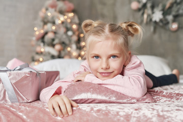 Fototapeta premium Merry Christmas and Happy Holidays! Cheerful cute child girl opening gifts. Kid wearing pajamas, having fun on christmas tree background in morning on bed. Christmas Family card