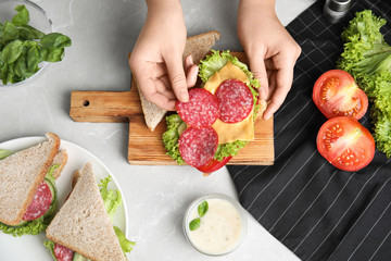 Woman making tasty sandwich with sausage at light grey marble table, top view