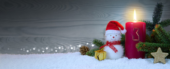 Christmas background with third Advent candle and Snowman with red decoration.