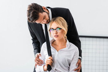Sexy businesswoman pulling tie of businessman in office