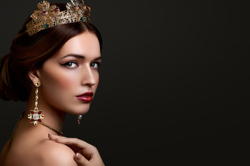 Close-up portrait beautiful girl with red lipstick in golden crown and earrings on dark background