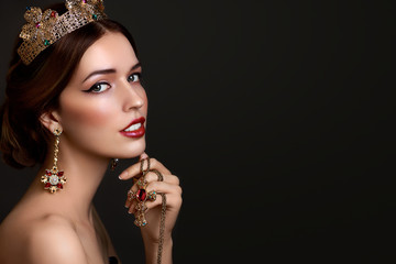 Beautiful girl with red lipstick in golden crown and earrings on dark background