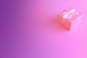 One gift or present box with a white ribbon bow on a pink and purple trend background. There is a place for text