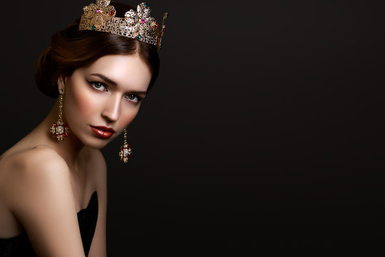 Close-up portrait beautiful girl with red lipstick in golden crown and earrings on dark background