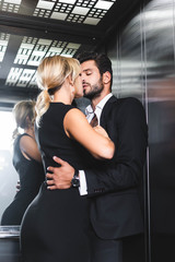 Business couple undressing while kissing in office elevator