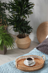 Fototapeta na wymiar Cup of coffee on bed in room decorated with green plants. Home design ideas