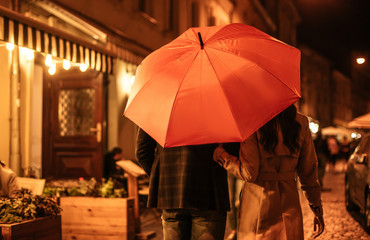 back view of couple in autumn outfit walking under umbrella along evening street