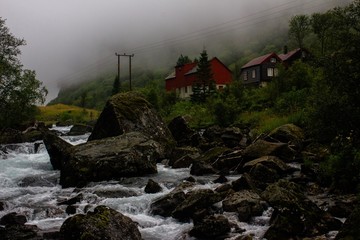 Fototapeta na wymiar Lonely houses by the river in a mountain gorge. Around fog, mountains and nearby passing railway. Norway