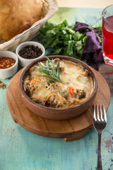 Braised beef with oven baked vegetables under cheese crust in clay bowl on blue wooden table