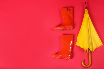 Beautiful yellow umbrella and rubber boots on red background, flat lay. Space for text