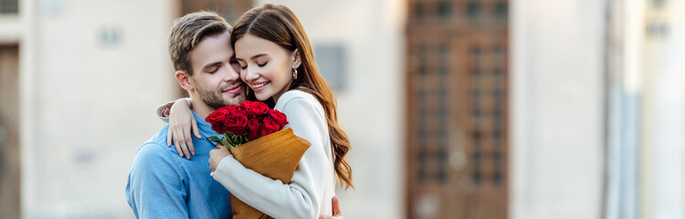 panoramic shot of happy girl embracing boyfriend while holding bouquet of roses - obrazy, fototapety, plakaty
