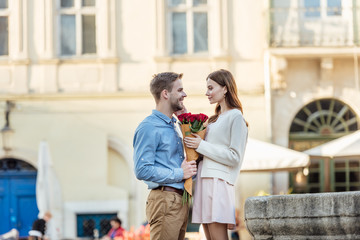 handsome man presenting bouquet of roses to happy girlfriend on street