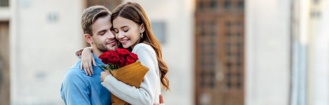 panoramic shot of happy girl embracing boyfriend while holding bouquet of roses