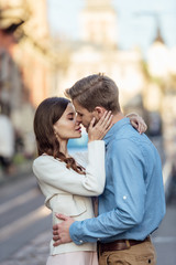 attractive young woman with closed eyes kissing handsome boyfriend on street