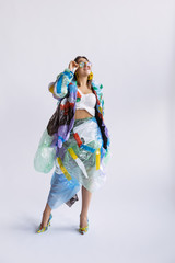 Woman wearing plastic on white background. Female model in clothes and shoes made of garbage. Fashion, style, recycling, eco and environmental concept. Too much pollution, we're eating and taking it.