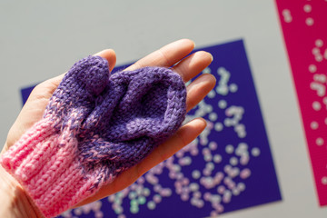 Children‘s  winter mittens  are on the female palm. Blue and pink  background with sequins. Handmade.