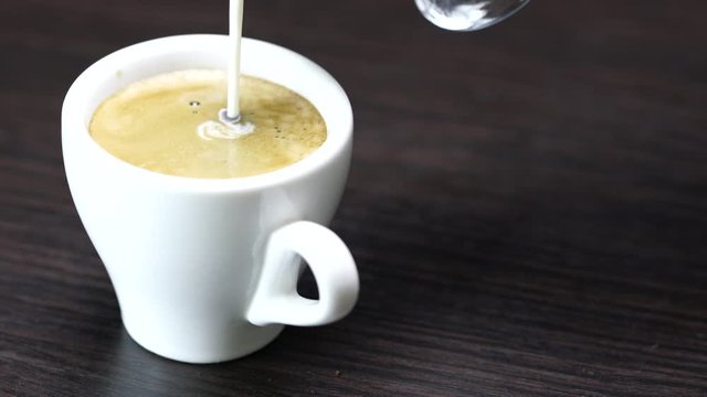 hot black coffee and cream is poured into a cup 